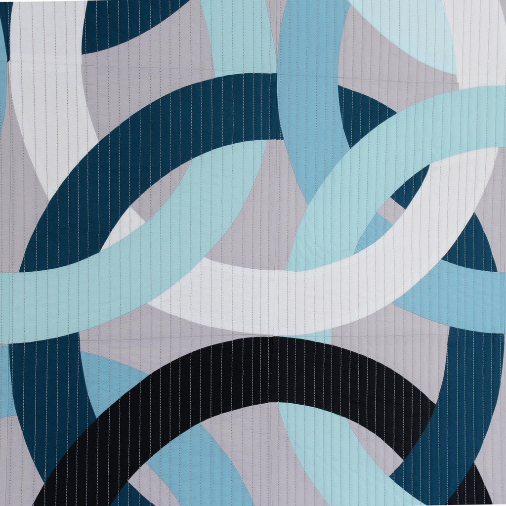 Close up of a geometric, modern, quilted wall hanging of interlocking rings in blue, black, and white on a gray background