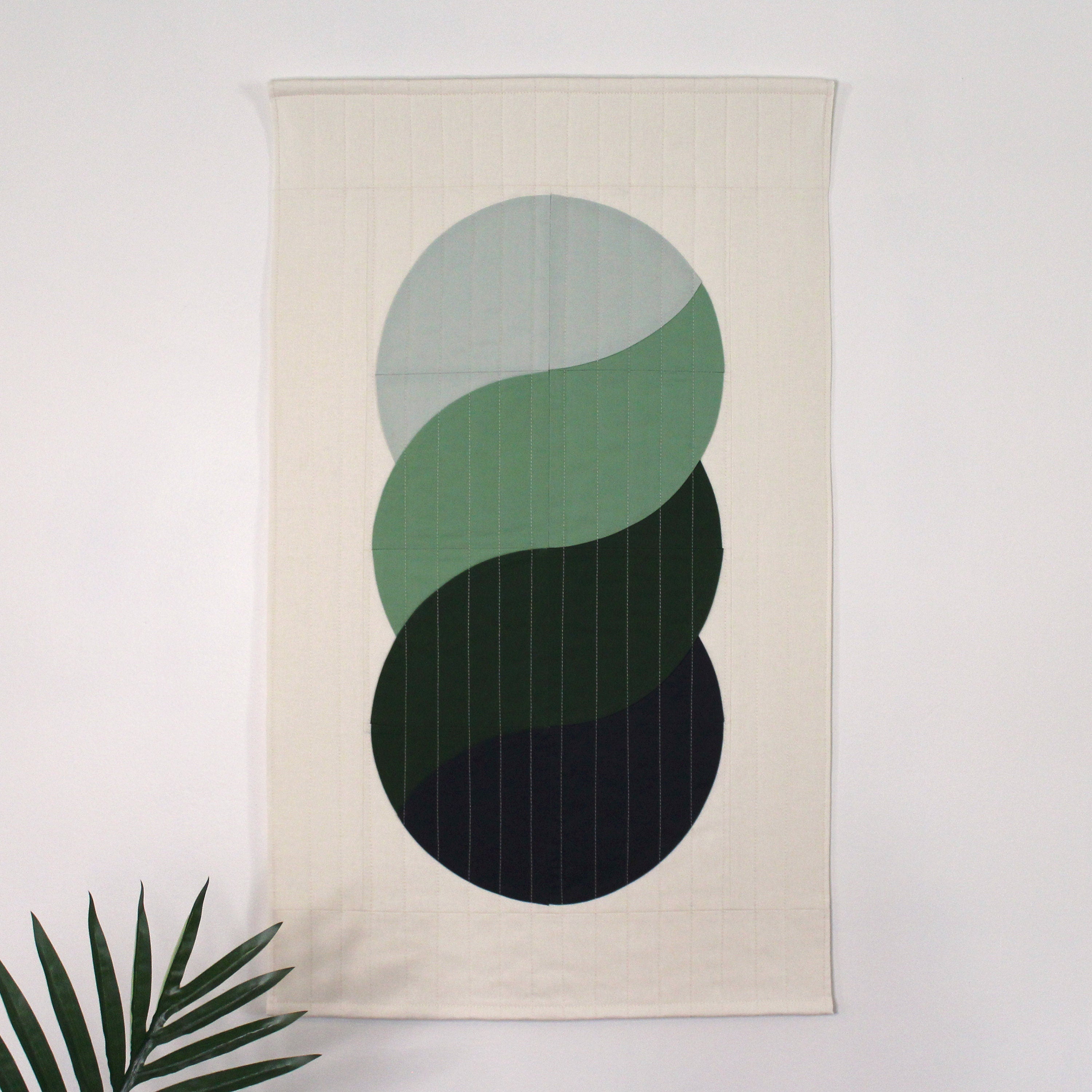 Decorative quilted wall hanging with interlocking swirls in shades of blues and greens, in a mid-century modern inspired design