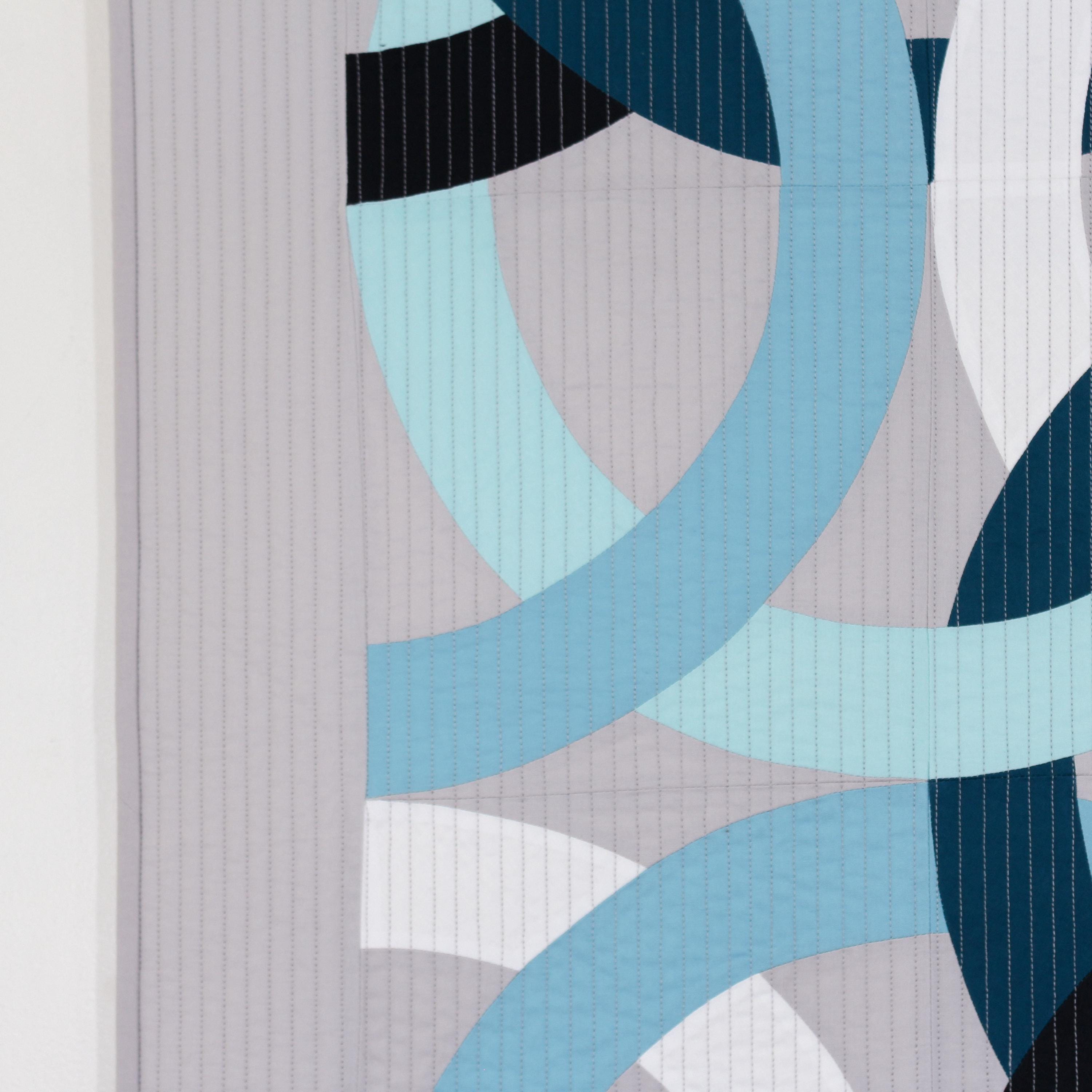 Geometric, modern, quilted wall hanging of interlocking rings in blue, black, and white on a gray background
