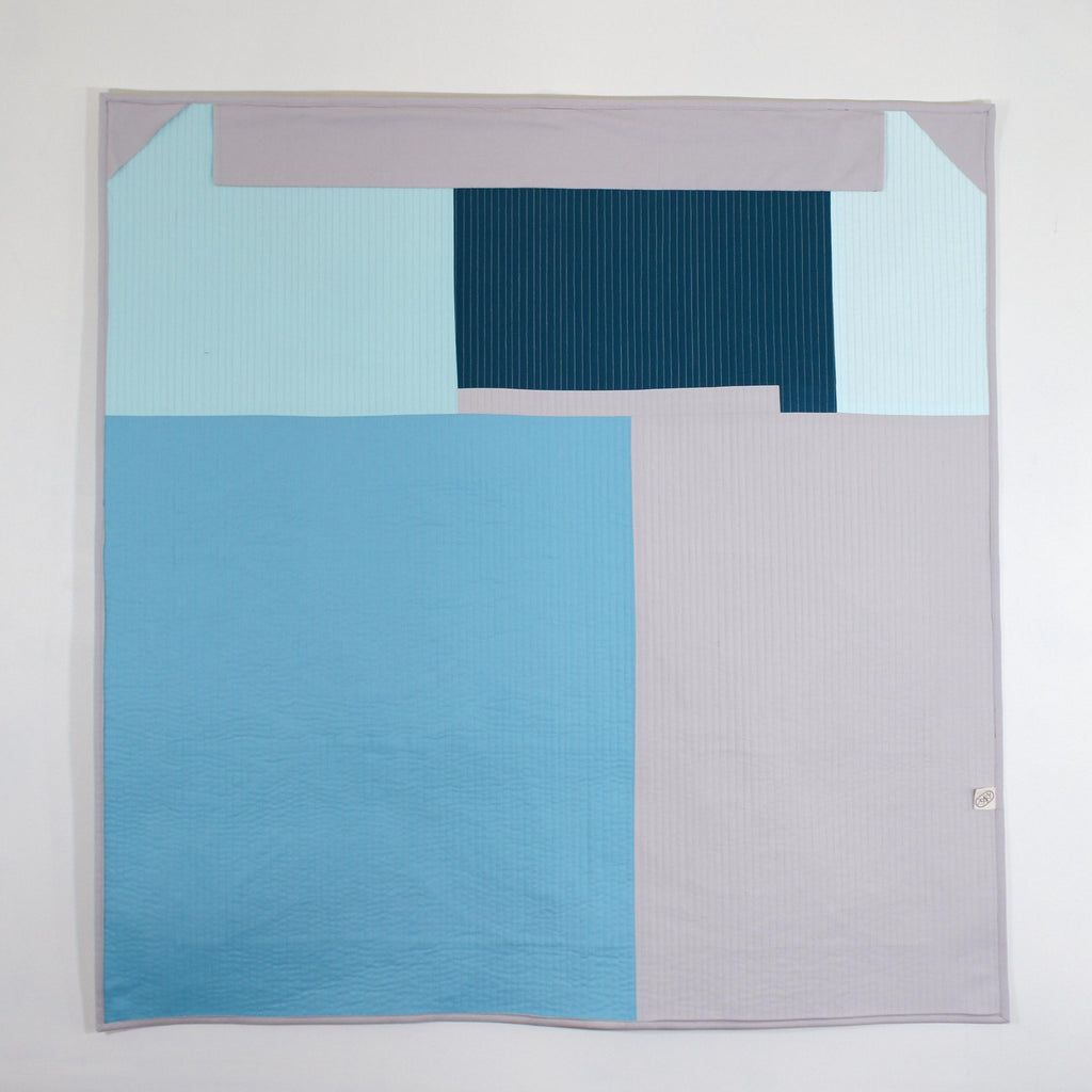 Backing of quilted wall hanging, showing a scrappy, geometric look in shades of blues and grey