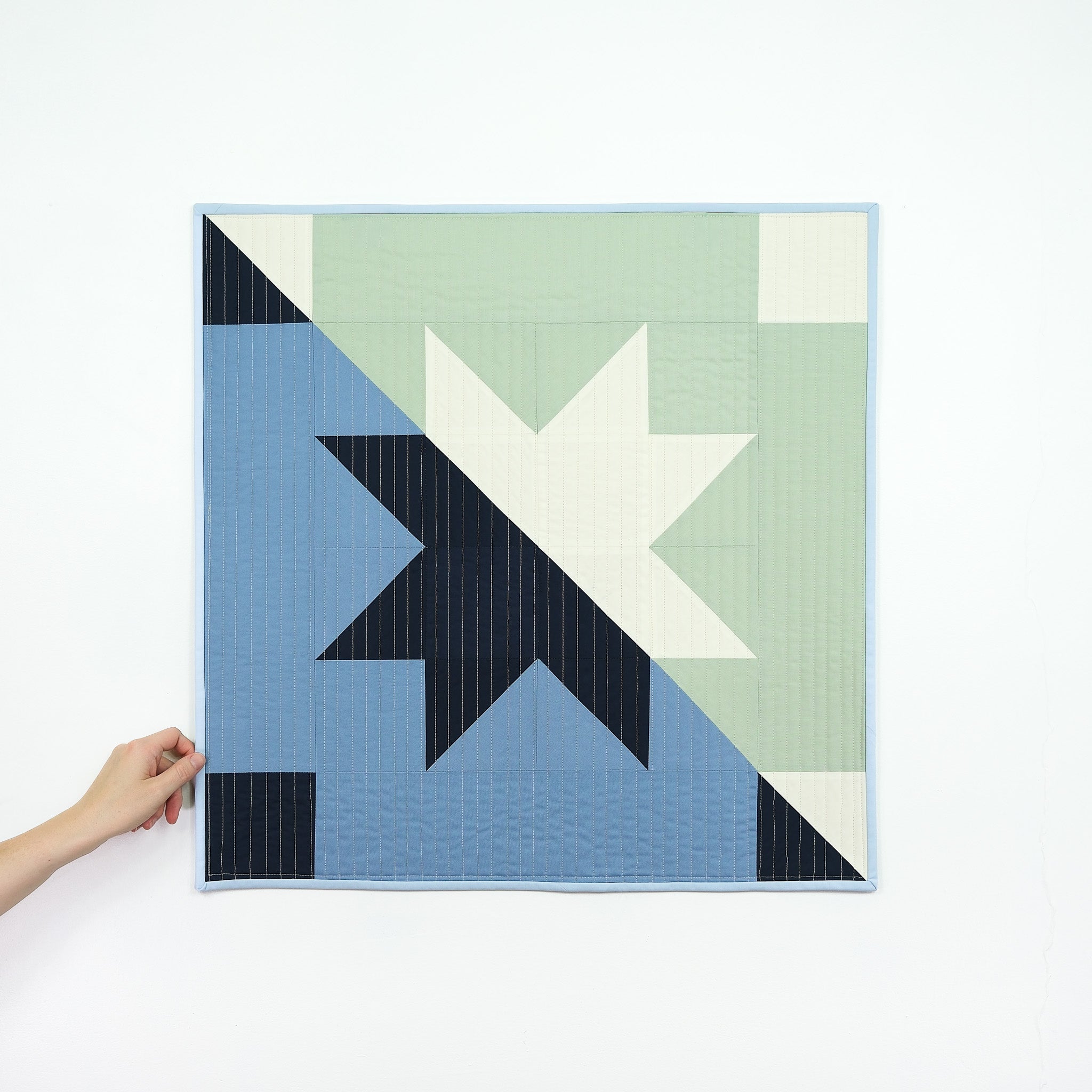 Quilt with geometric star design held by a hand on a white background