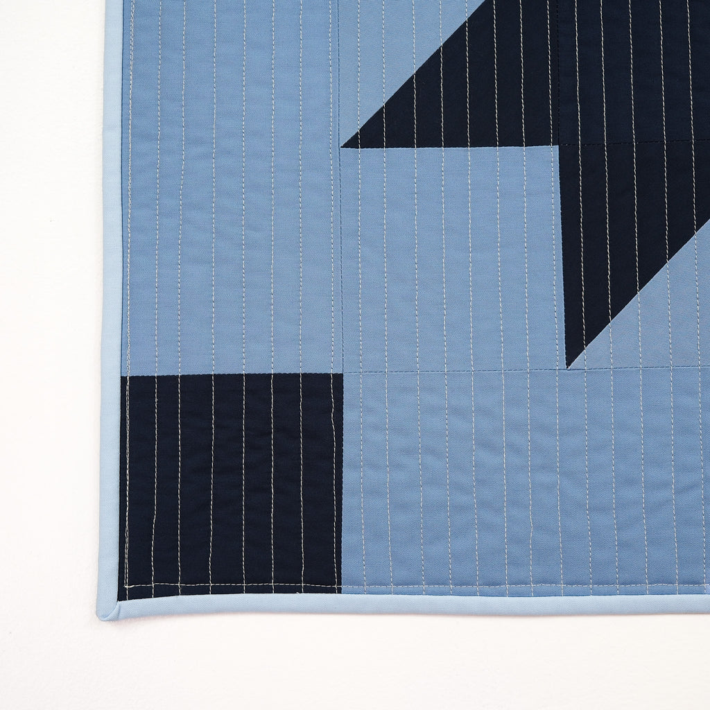 Blue quilt with black geometric patterns on a white background