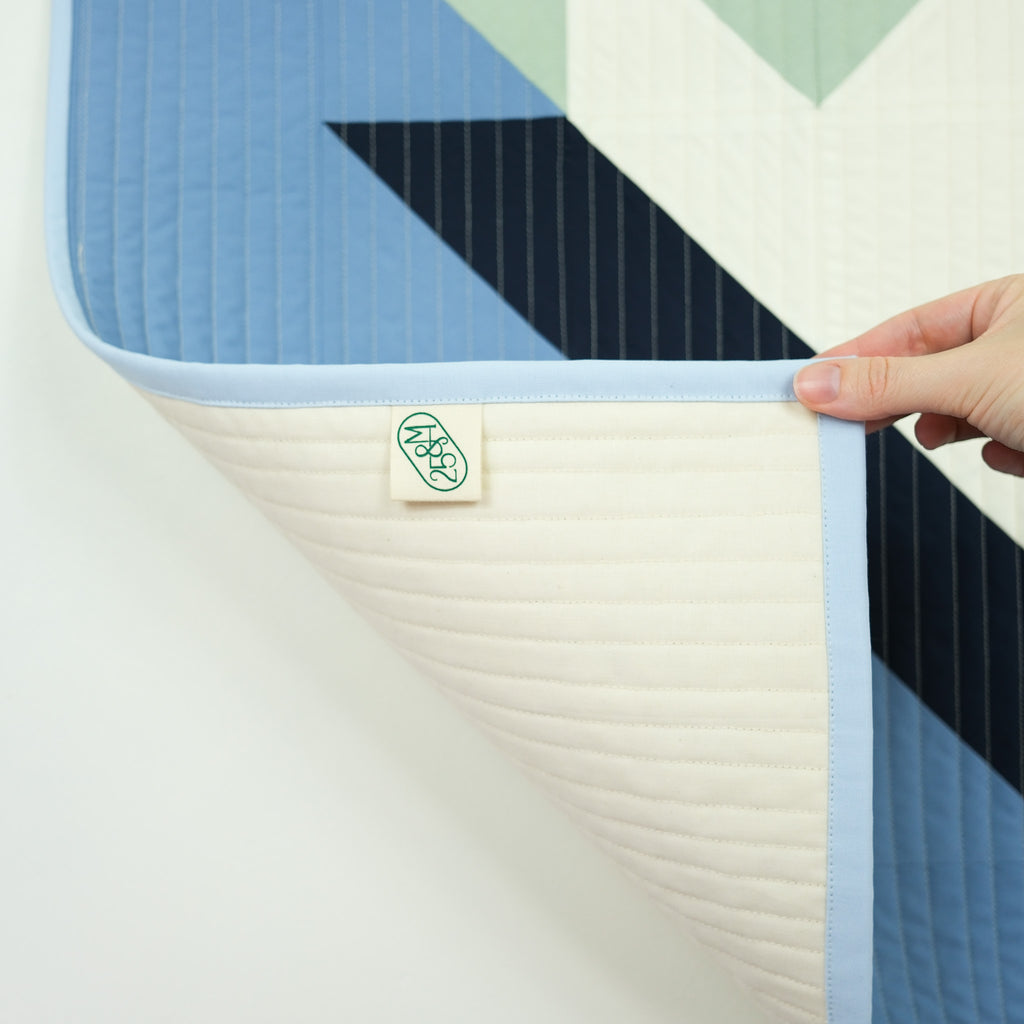 Colorful quilt with geometric pattern held by a hand, featuring a brand tag.