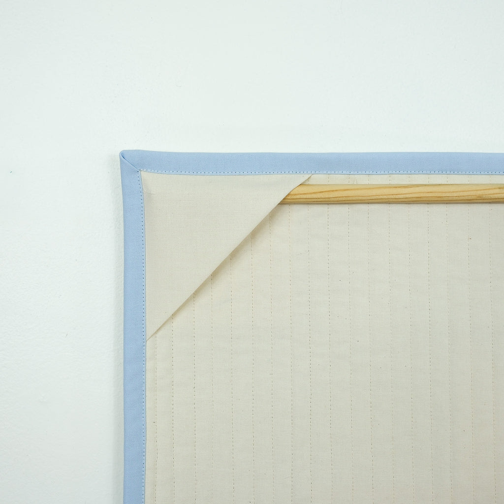 Backing of hanging quilt showing corner tabs with a wooden dowel