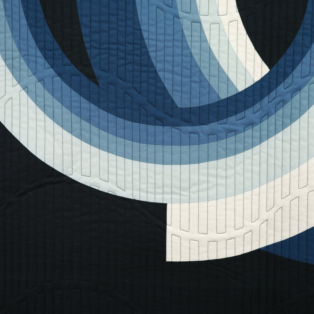 Close-up of a quilt with concentric circle pattern in blue and white on a black background