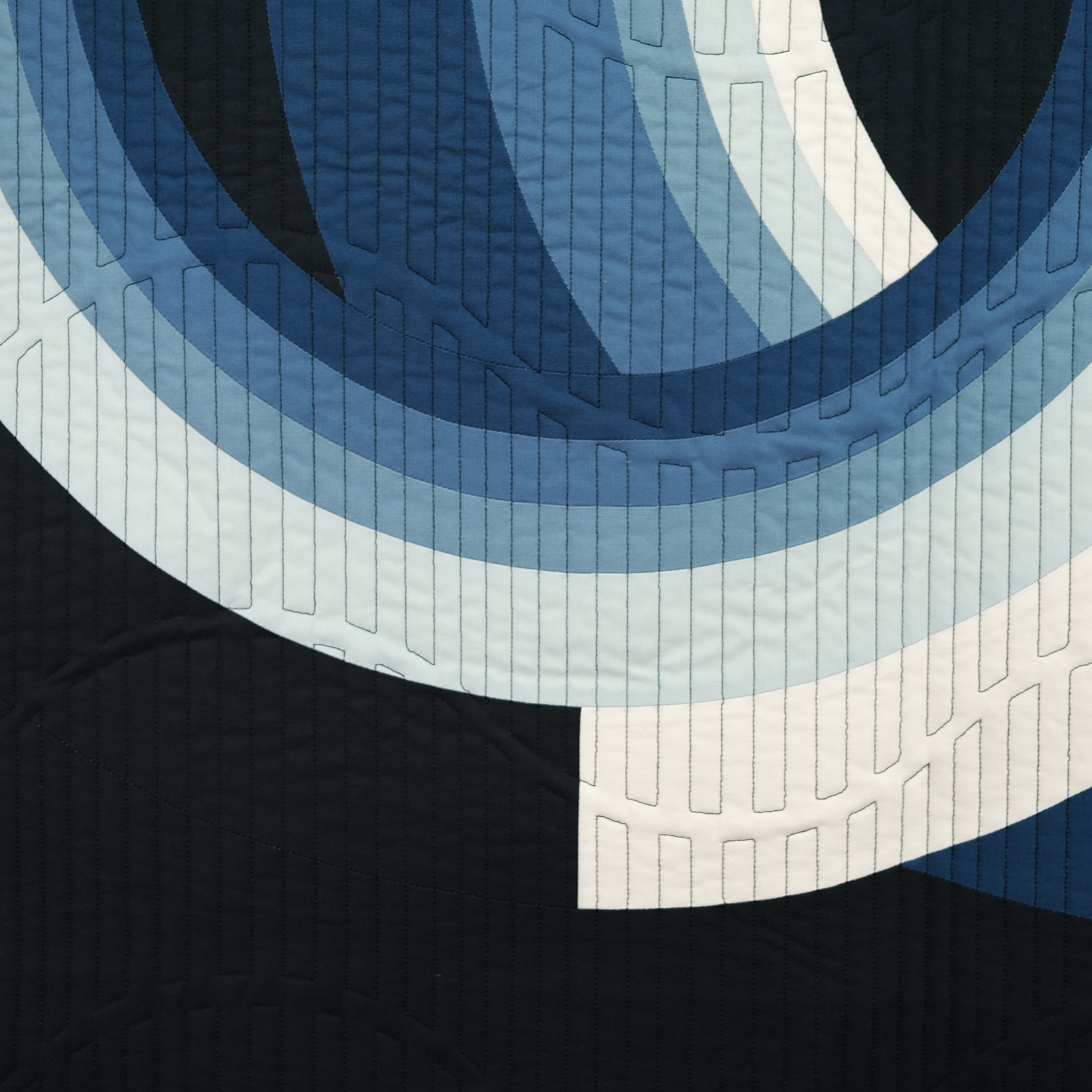 Close-up of a quilt with concentric circle pattern in blue and white on a black background