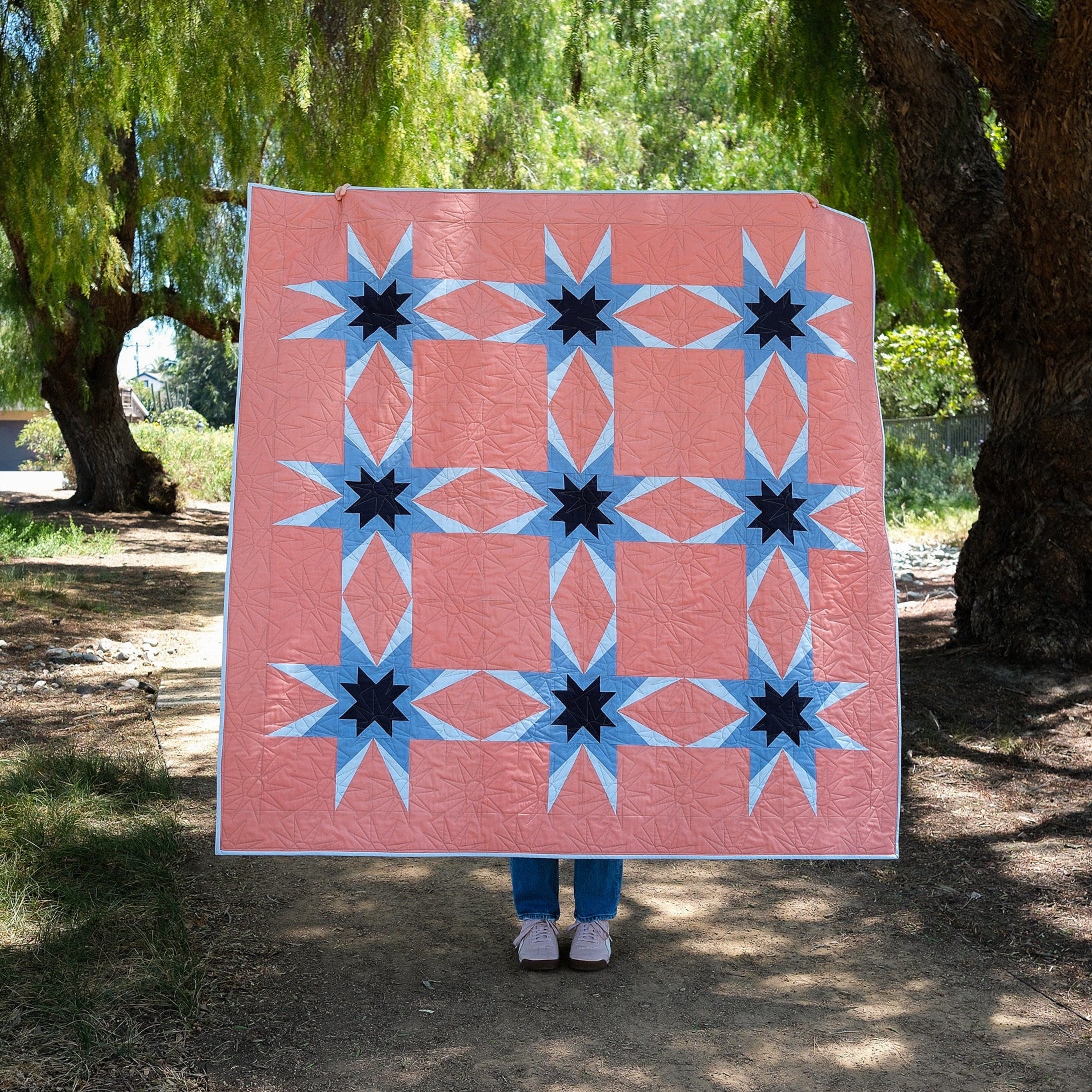 Person holding a pink quilt with star patterns in a park setting