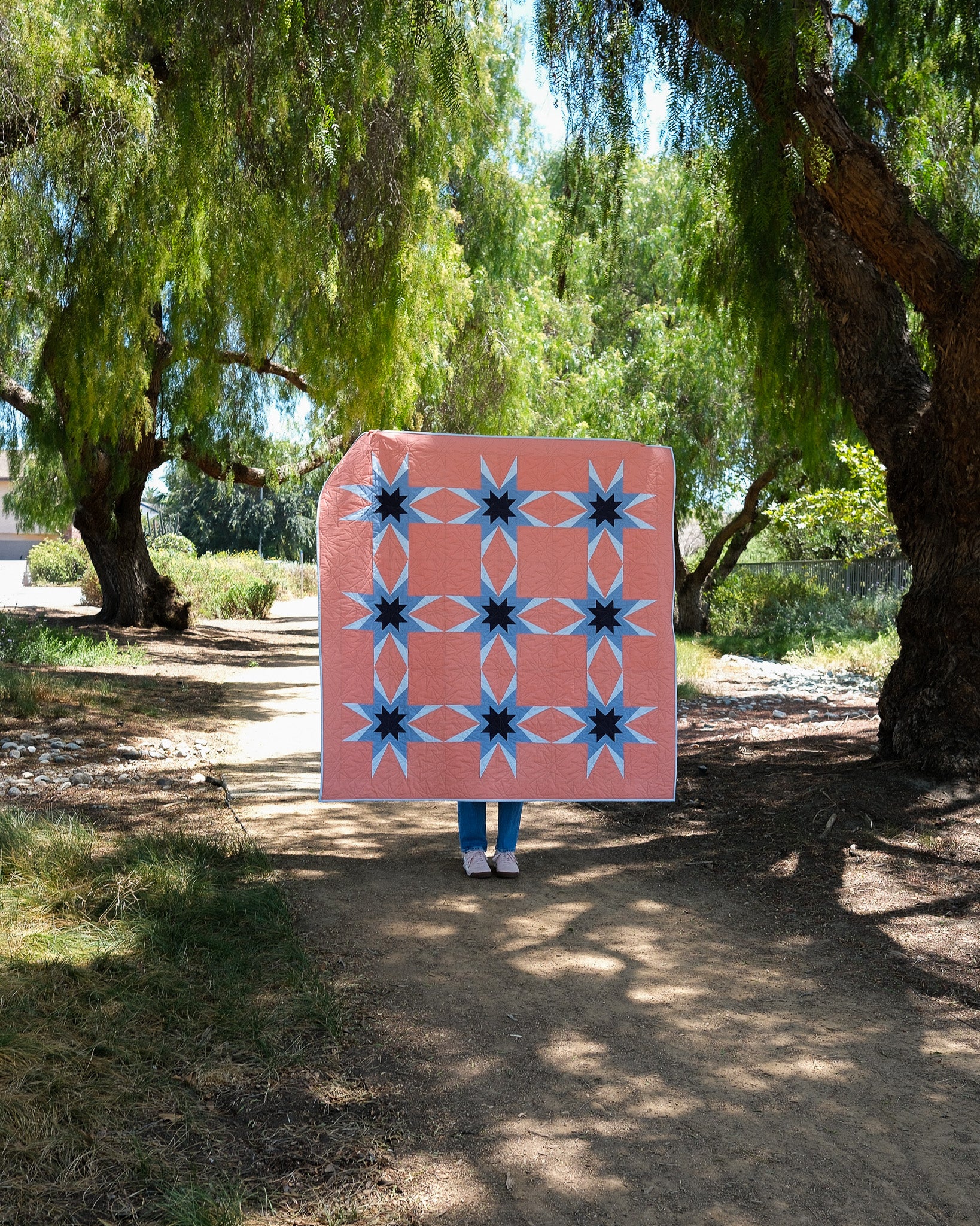 Person holding a quilt with geometric pattern in a sunlit outdoor setting