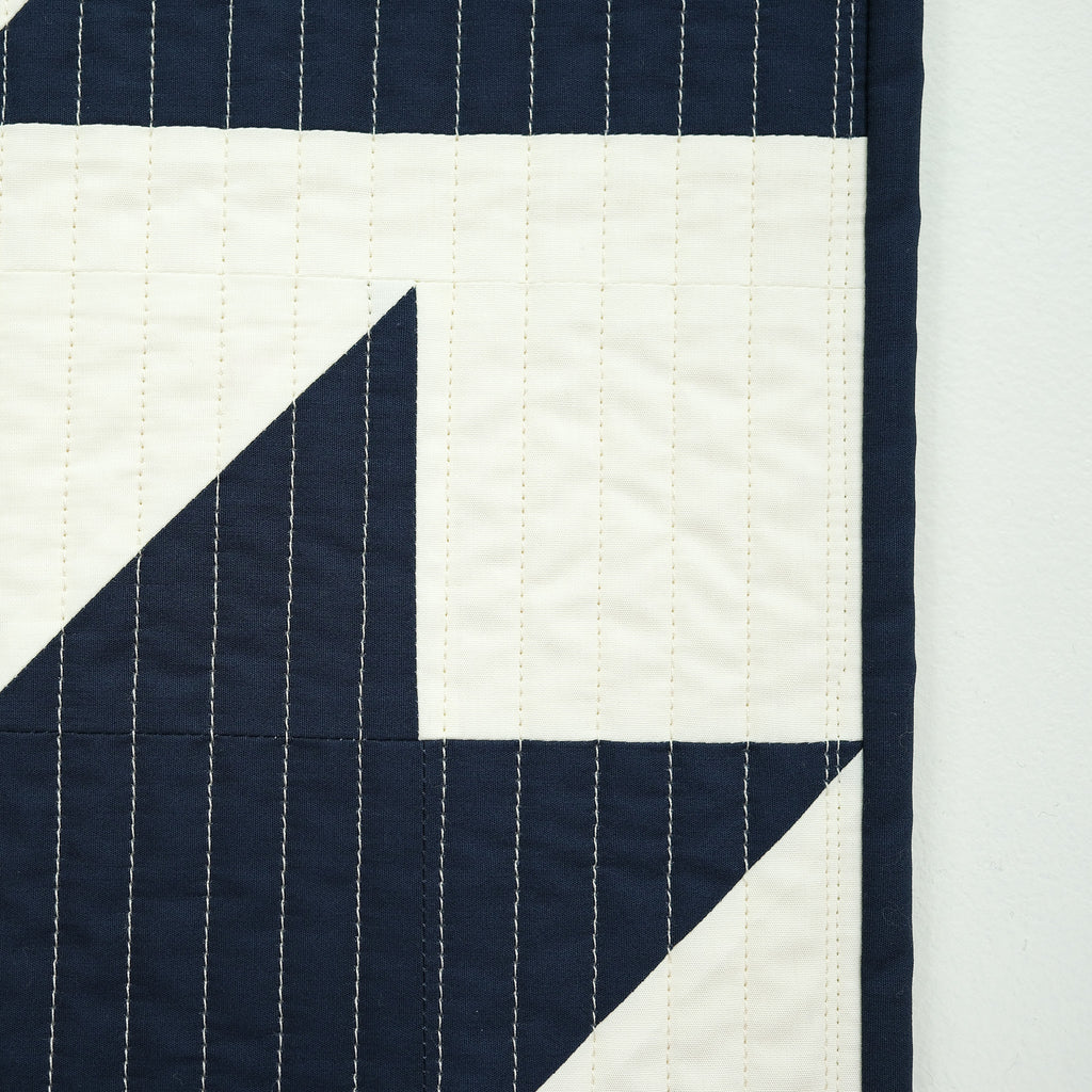 Navy and white quilt with geometric pattern on a light gray background