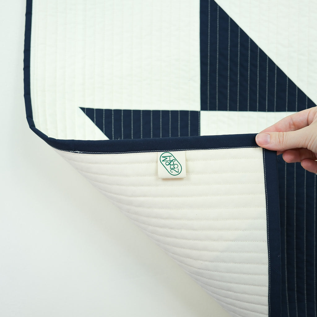 Navy and white quilt with a brand label on a light background