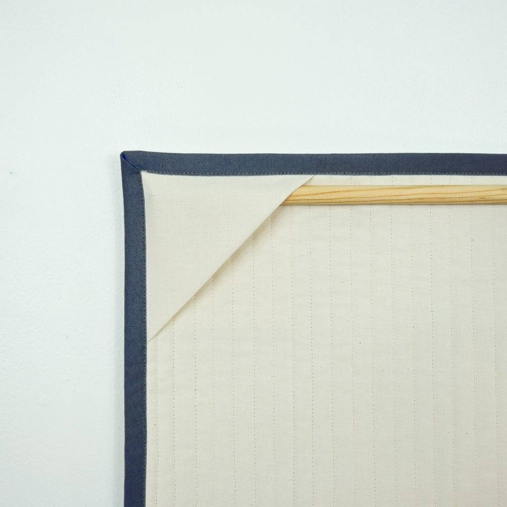 Backing of hanging quilt showing corner tabs with a wooden dowel