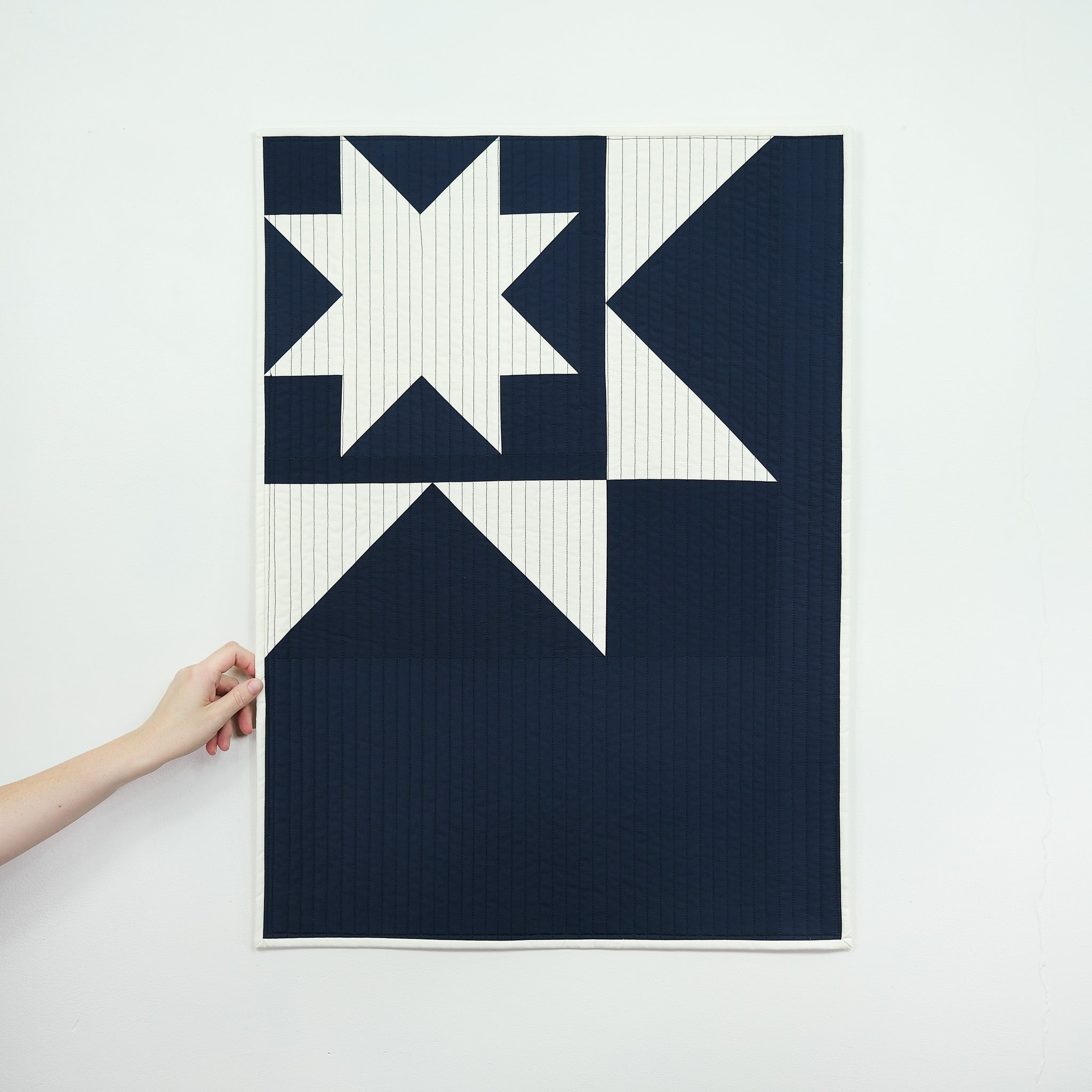 Navy and white quilt with geometric pattern held by a hand on a light gray background
