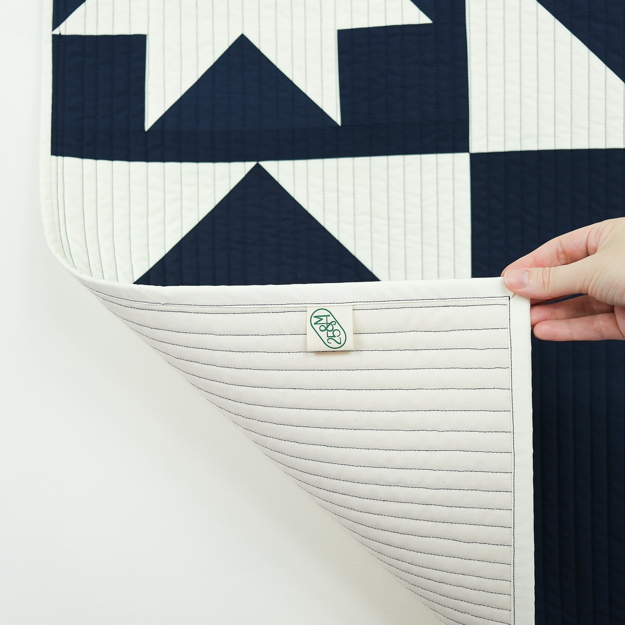 Navy and white patterned quilt with a brand label held by a hand on a light gray background