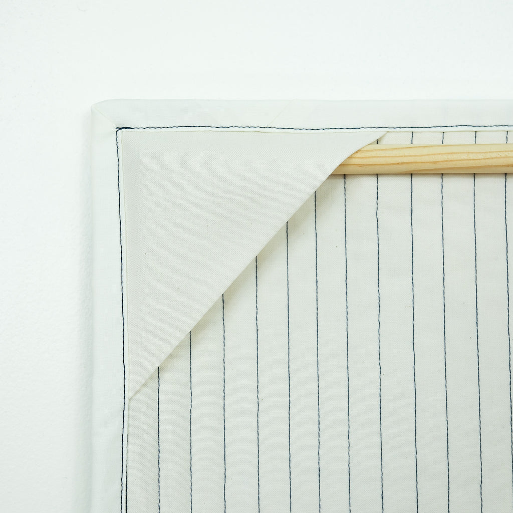 Backing of hanging quilt showing corner tabs with a wooden dowel
