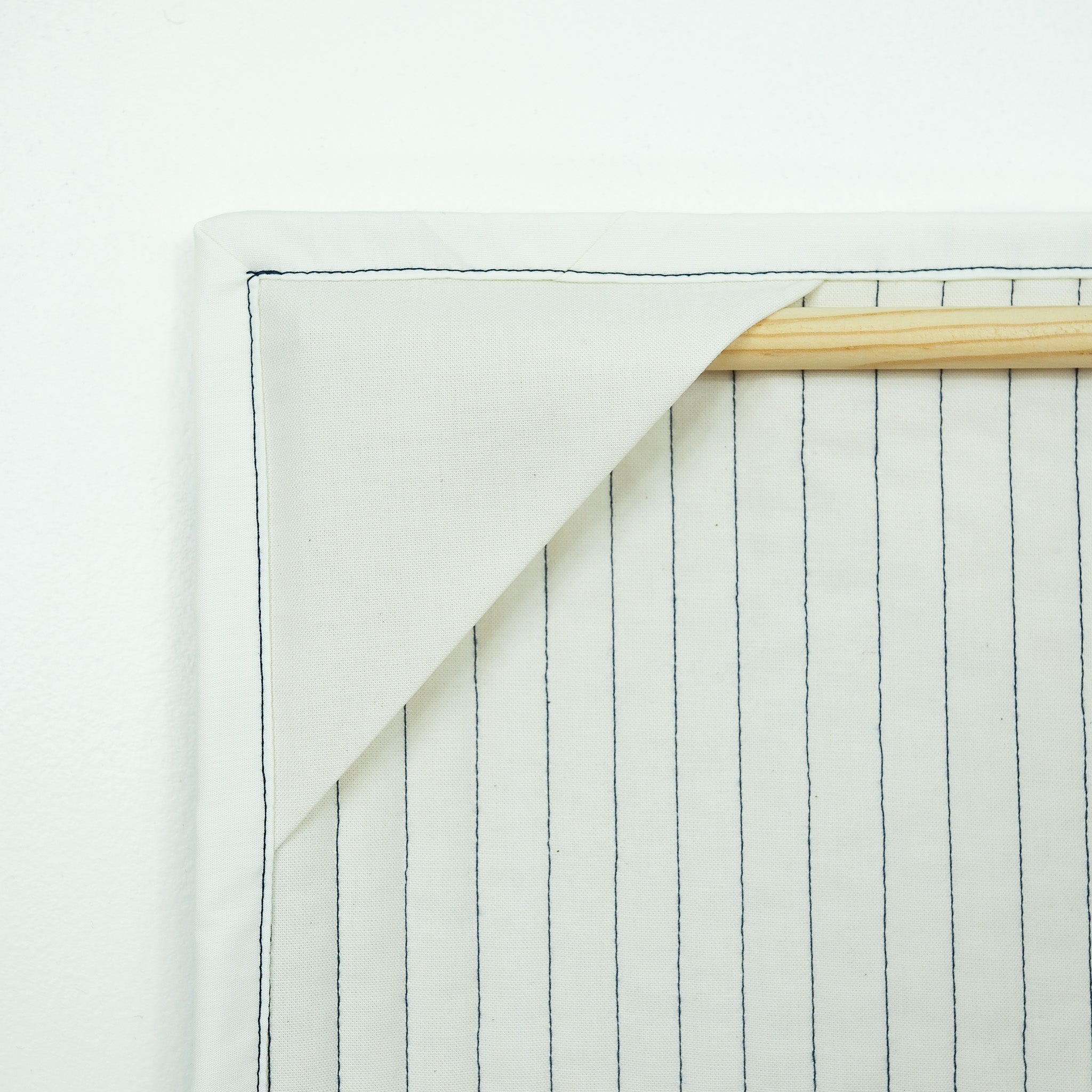 Backing of hanging quilt showing corner tabs with a wooden dowel