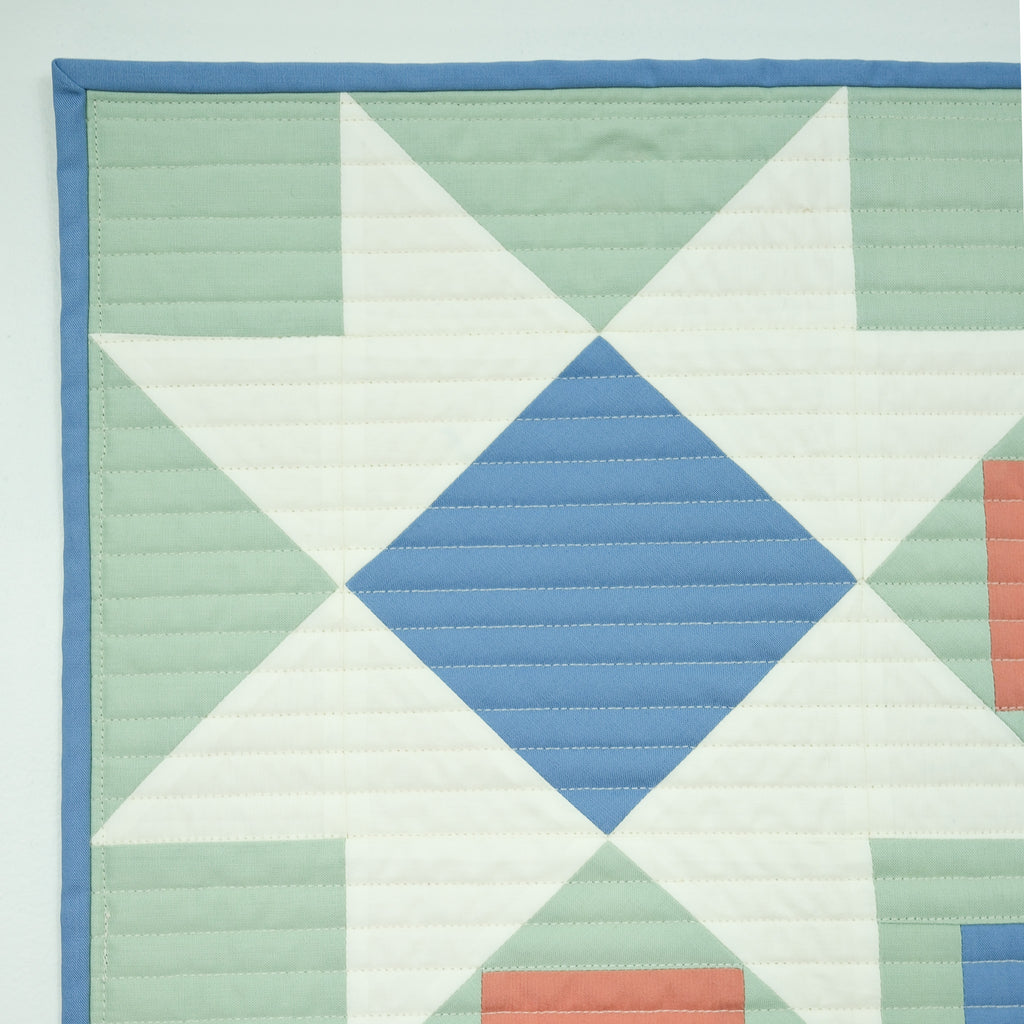 Quilt with geometric pattern featuring triangles and a diamond shape in pastel colors on a light blue background.