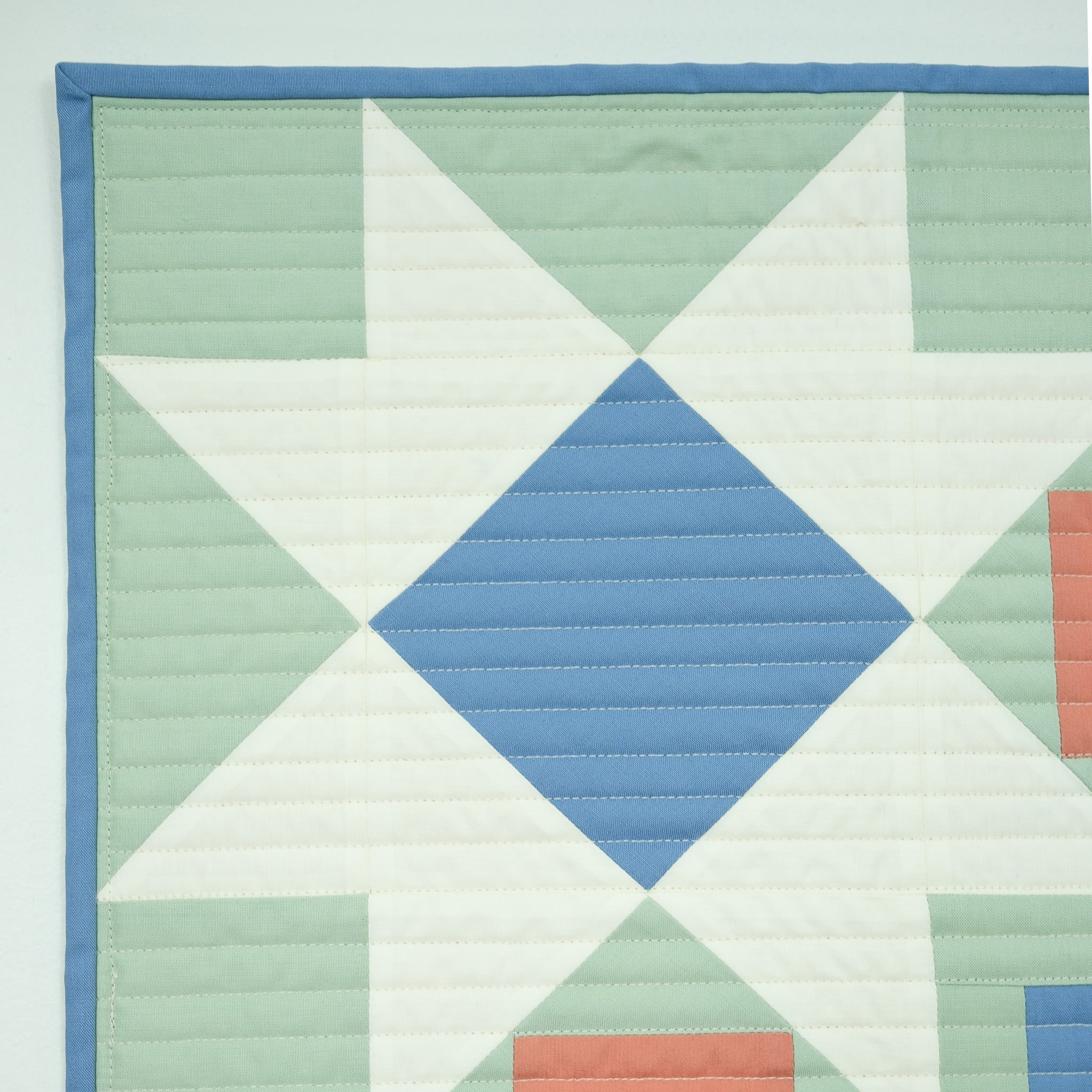 Quilt with geometric pattern featuring triangles and a diamond shape in pastel colors on a light blue background.