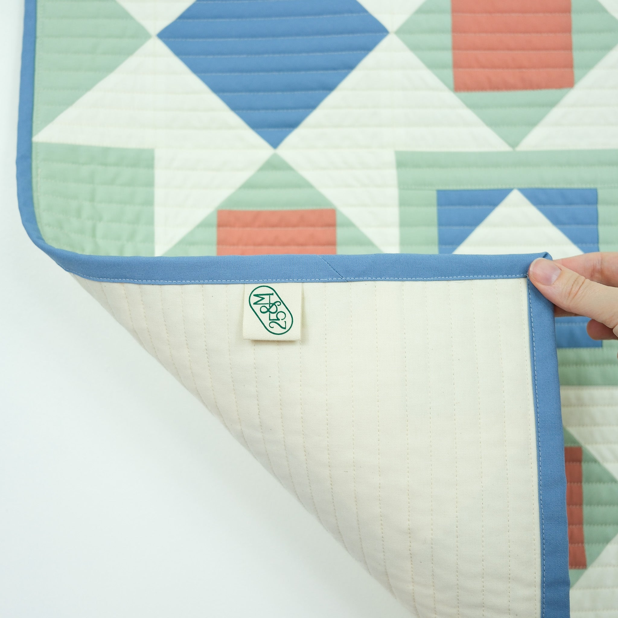 Colorful geometric-patterned quilt with a hand holding it on a white background