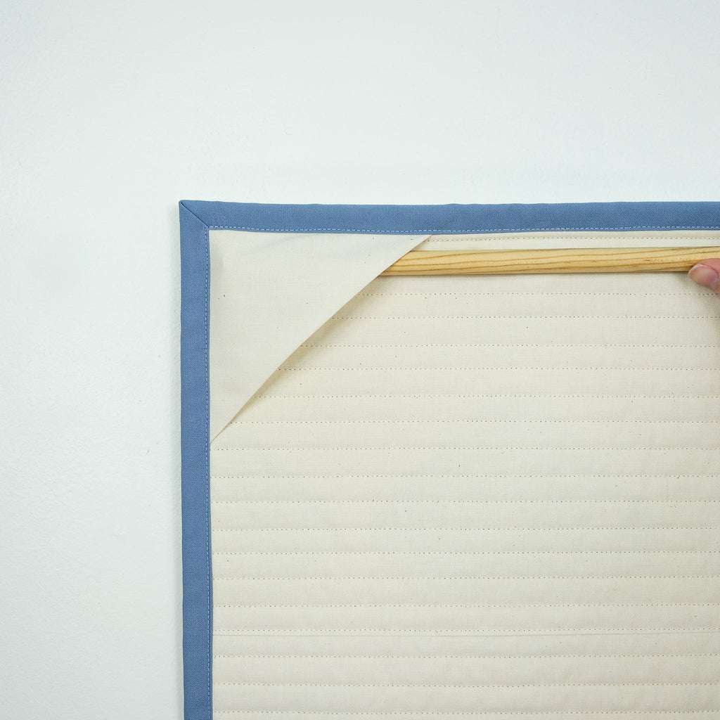 Backing of hanging quilt showing corner tabs with a wooden dowel