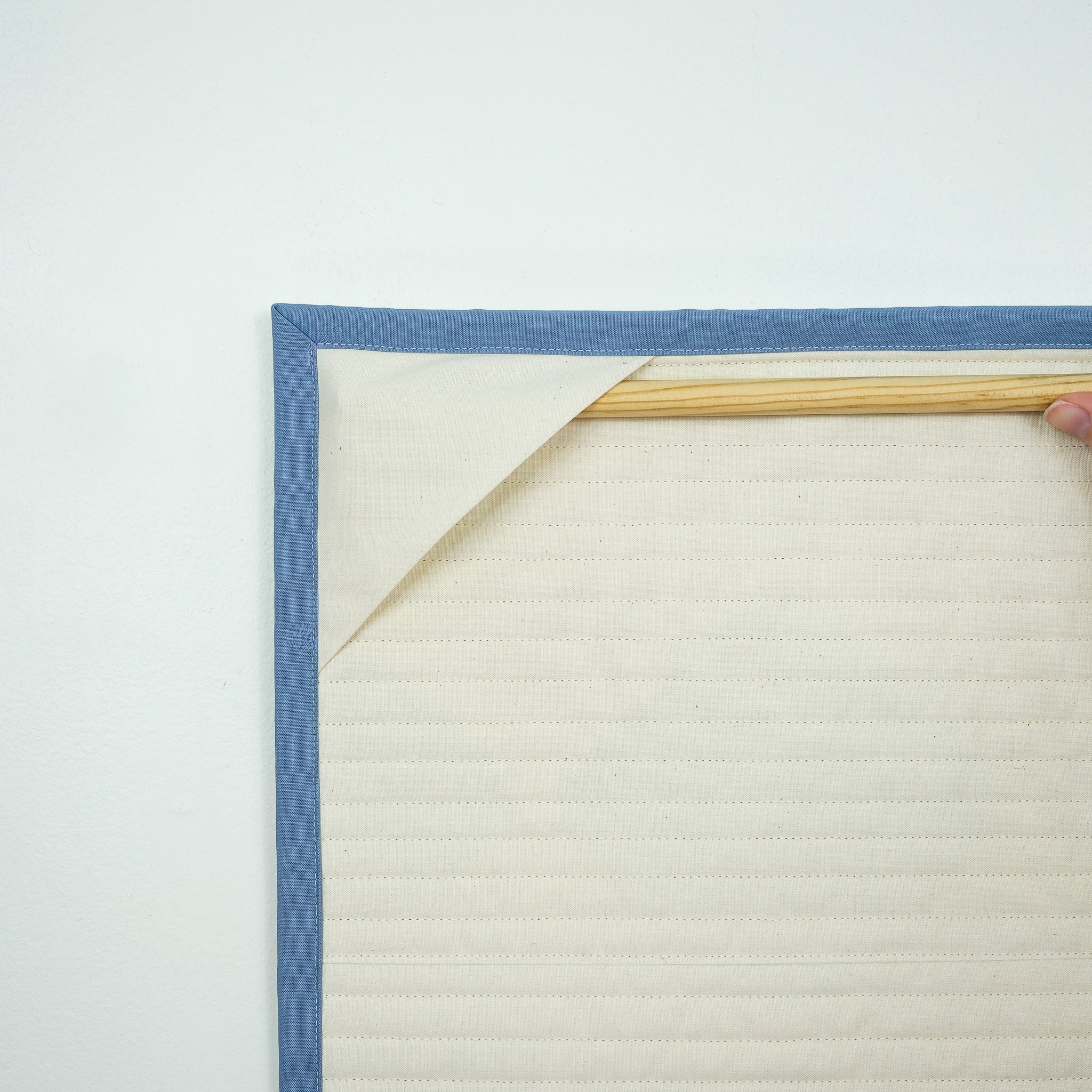 Backing of hanging quilt showing corner tabs with a wooden dowel