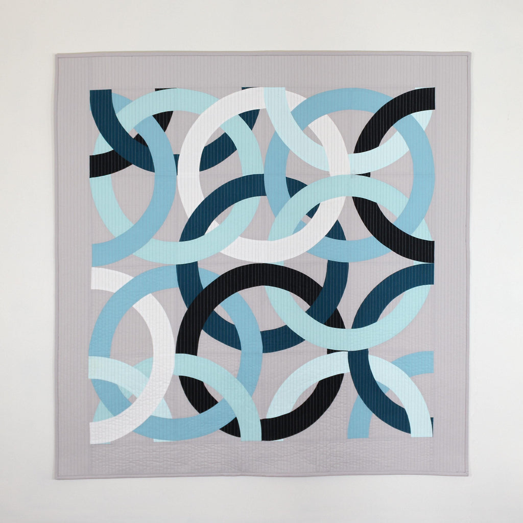 Geometric, modern, quilted wall hanging of interlocking rings in blue, black, and white on a gray background