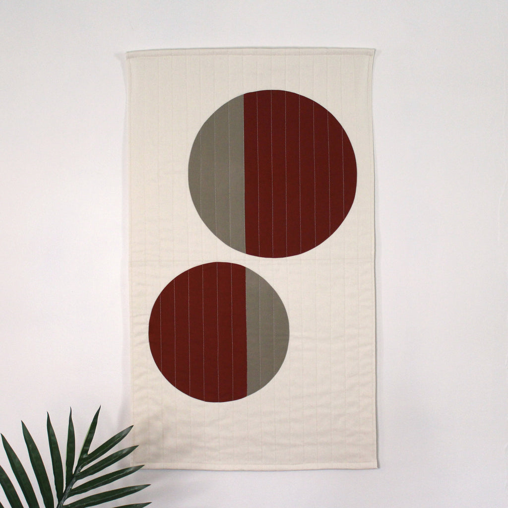 Geometric modern quilted wall hanging with a beige and rust color palette, with abstract circle design