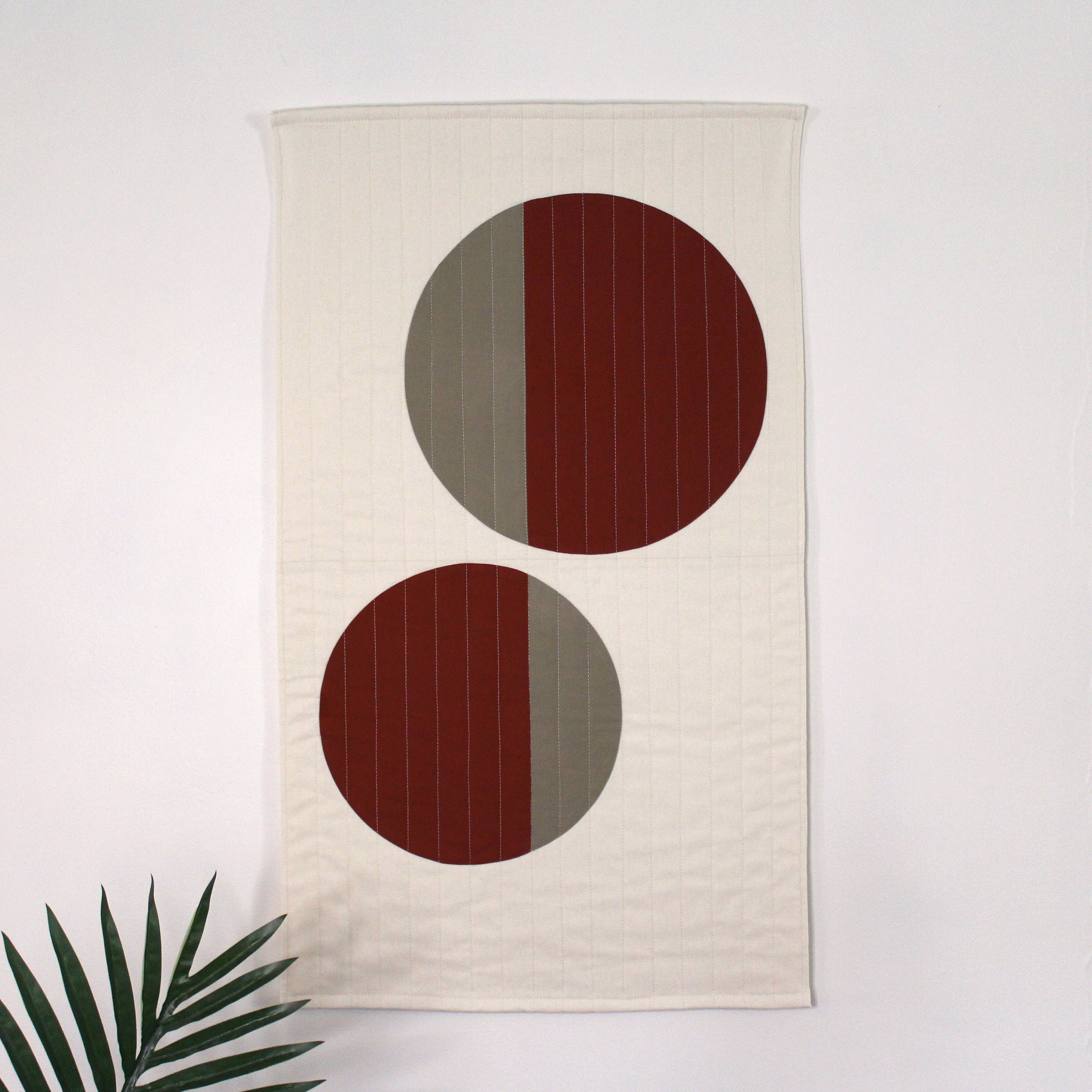 Geometric modern quilted wall hanging with a beige and rust color palette, with abstract circle design