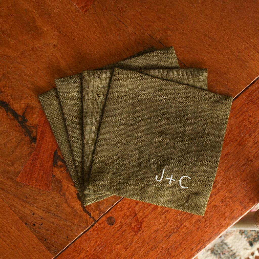 Set of green napkins with 'J+C' embroidery on a wooden surface